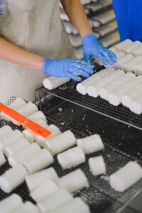 A worker in gloves arranges cheese blocks on racks in a factory setting, showcasing food production.